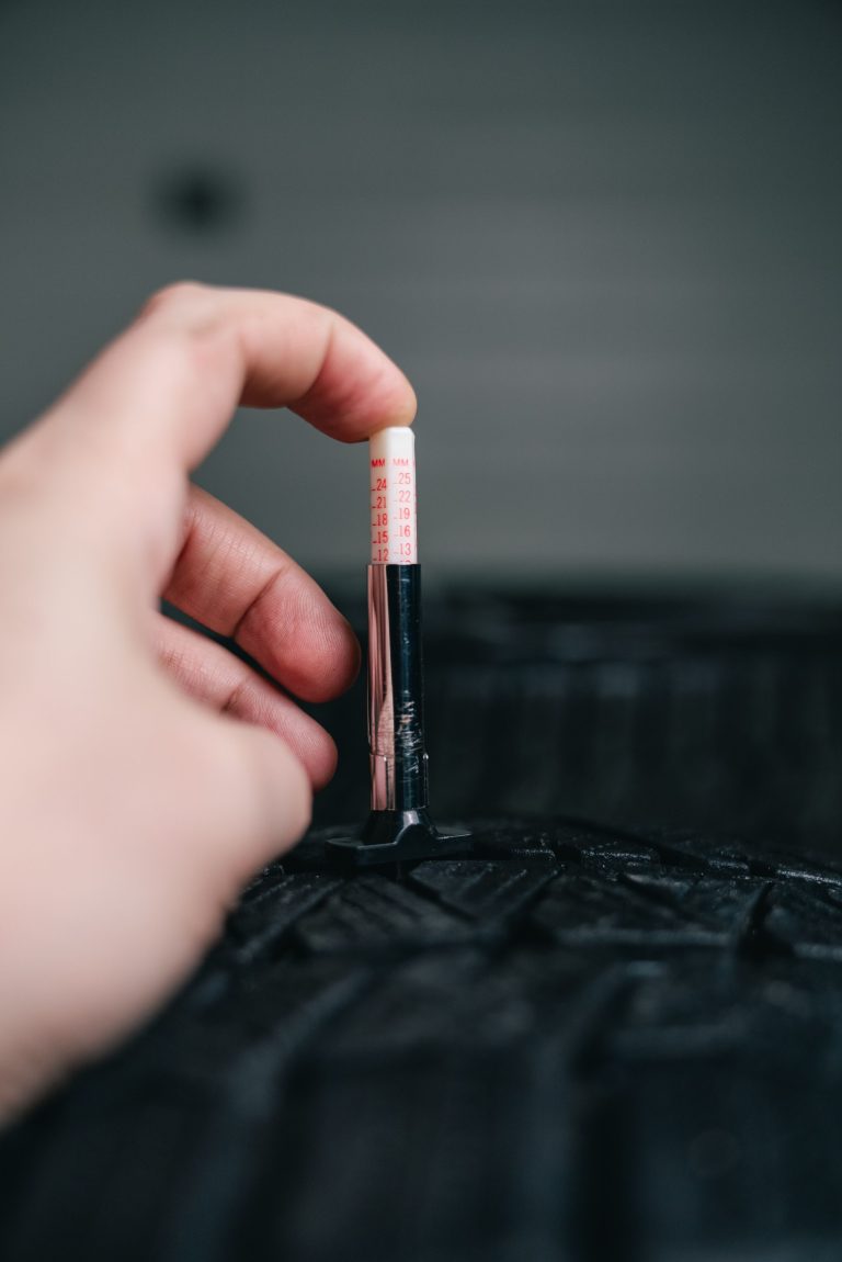 Close-up of hand using a tread depth gauge on a tire. Safety and maintenance check. Gros plan de la main utilisant un jauge de profondeur de bande de roulement sur un pneu. Vérification de la sécurité et de l'entretien.