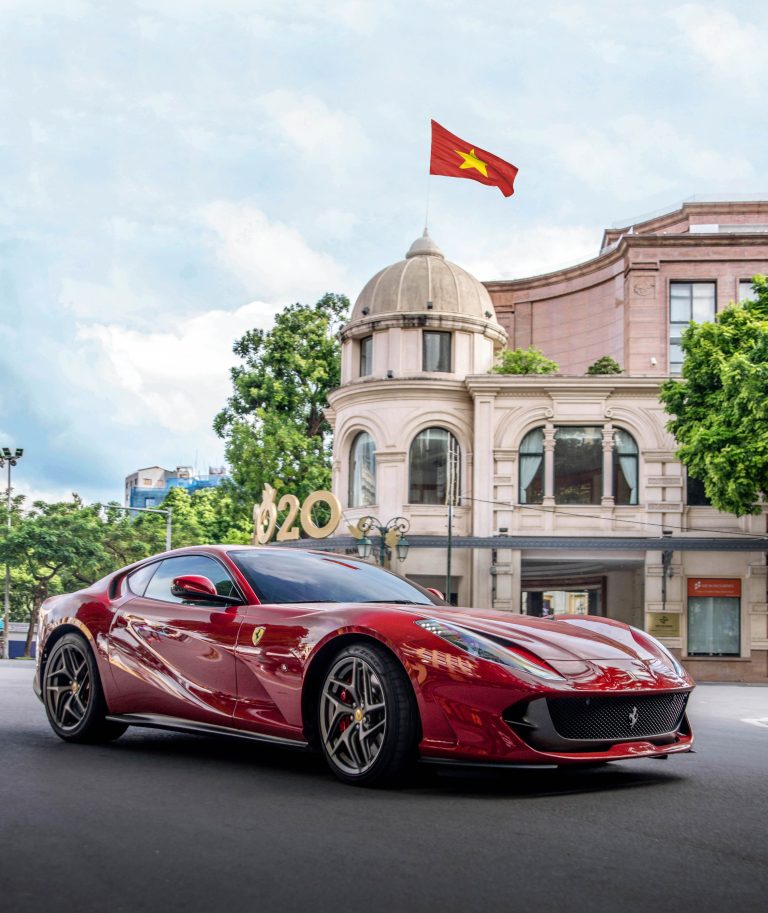 A red luxury sports car parked in front of a historic building in Hanoi, Vietnam. Une voiture de sport de luxe rouge garée devant un bâtiment historique à Hanoï, au Vietnam.