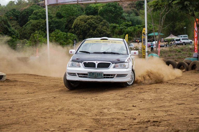 A rally car kicks up dust while drifting on a dirt track during a racing event. Une voiture de rallye soulève la poussière en dérapant sur une piste de terre lors d'un événement de course.
